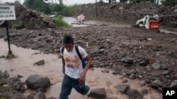 ARCHIVO - Un hombre cruza un arroyo en una carretera después de que un río se desbordó en Verapaz, El Salvador, el domingo 30 de mayo de 2010.