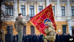 Rais wa Ukrain Volodymyr Zelenskyy akiwa amebeba bendera ya kijeshi huku mwanajeshi akiipiga busu wakati wa maadhimisho ya mwaka mmoja wa uvamizi wa Russia. Feb. 24, 2023. 