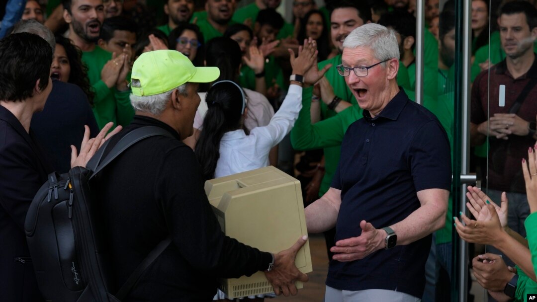 Apple CEO Tim Cook, right, reacts after seeing an old old Macintosh Classic machine brought by a visitor during the opening of the first Apple Inc. flagship store in Mumbai, India, April 18, 2023.