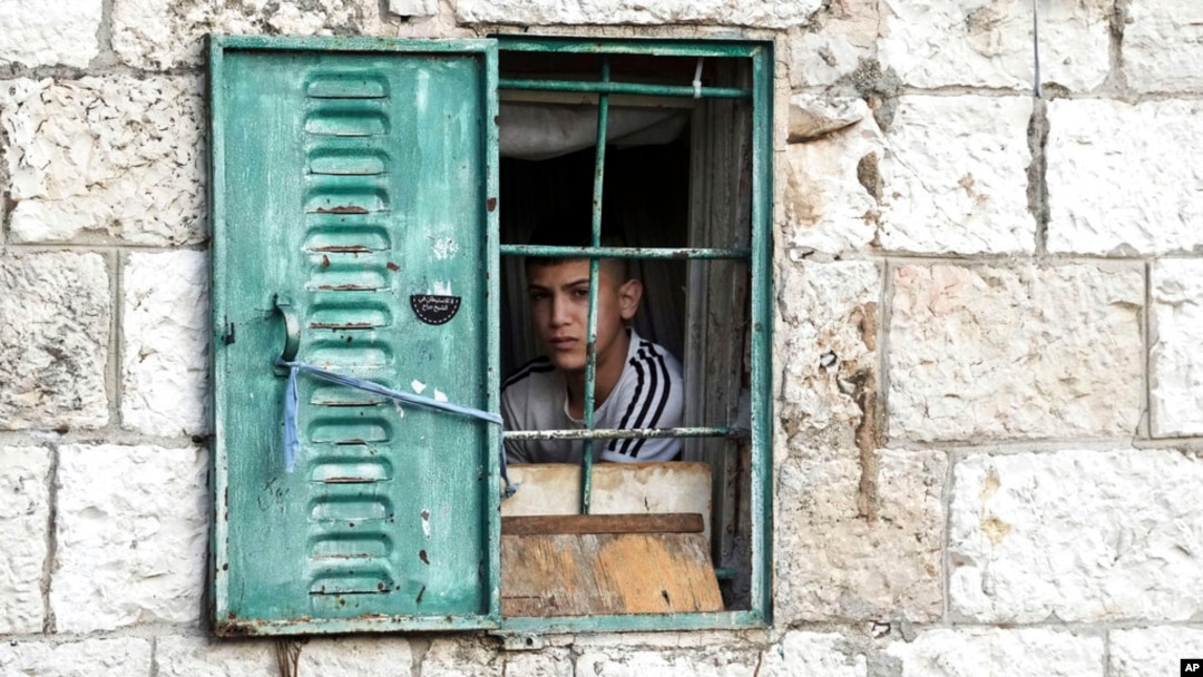 ARCHIVO - Un joven palestino observa desde su ventana una manifestación semanal en solidaridad con los residentes del barrio Sheikh Jarrah en Jerusalén oriental, donde las familias palestinas están bajo amenaza inminente de desplazamiento forzado, el viernes 7 de enero de 2022.