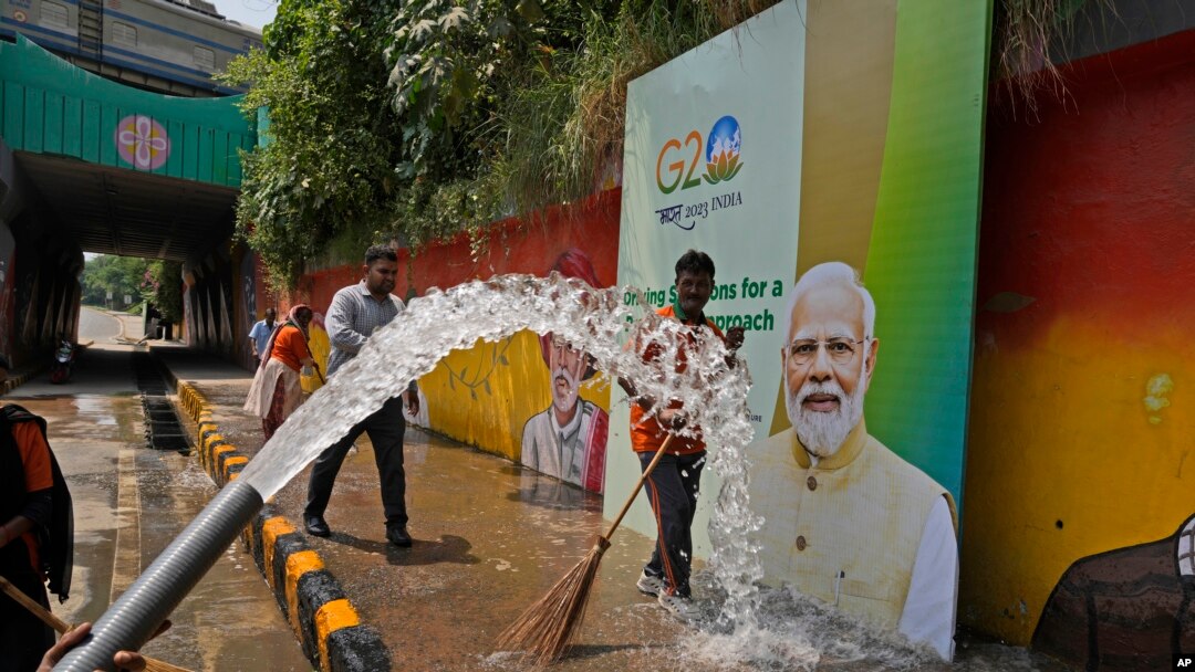 Municipal workers wash a side walk near a billboard featuring Indian Prime Minister Narendra Modi ahead of this week's summit of the Group of 20 nations, in New Delhi, India, Sept. 7, 2023.