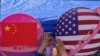 A vendor tights a flowers deco in between of the planets shaped of China and American flags on display at a store during a Spring Carnival in Beijing on May 13, 2023. (AP Photo/Andy Wong)