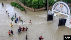 Peões atravessam uma rua inundada na sequência de fortes chuvas no distrito de Kiembeni, em Mombaça, Quénia, a 17 de novembro de 2023.