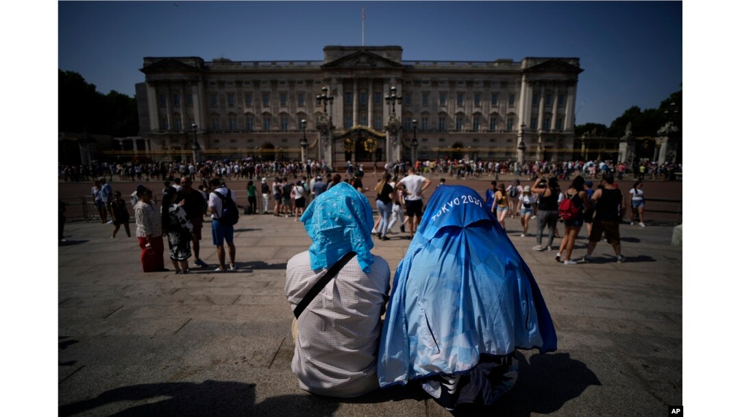 People sit covering their heads from the sun after a scaled down version of the Changing of the Guard ceremony took place outside Buckingham Palace, during hot weather in London, Monday, July 18, 2022. (AP Photo/Matt Dunham)
