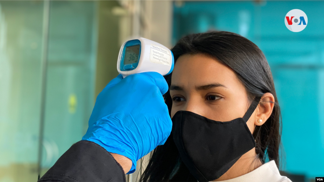 Un oficial de seguridad mide la temperatura a una trabajadora nicaragüense. Foto Houston Castillo, VOA.