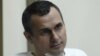FILE - Oleg Sentsov sits behind glass in a cage at a court room in Rostov-on-Don, Russia, July 21, 2015. 