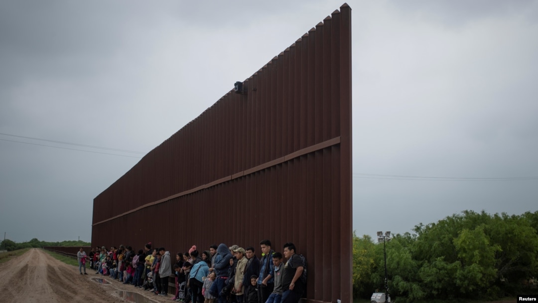 Migrantes centroamericanos se alinean a lo largo del muro fronterizo mientras esperan rendirse a la patrulla fronteriza de EE.UU., 2 de abril de 2019.