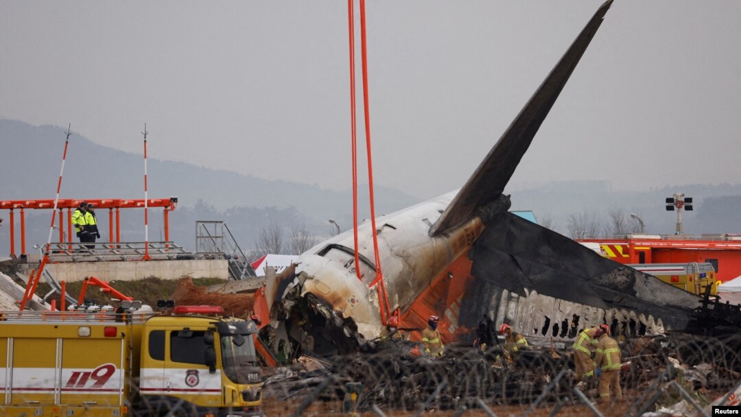 FILE - People stand as the wreckage of an aircraft lying on the ground after it went off the runway and crashed at Muan International Airport is pictured, in Muan, South Korea, Dec. 30, 2024. 