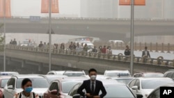 People wearing face masks walk past cars clogged with heavy traffic on a road as Beijing is hit by polluted air and sandstorm, May 4, 2017. Authorities in Beijing issued a blue alert on air pollution as sandstorm swept through the Chinese capital city on 