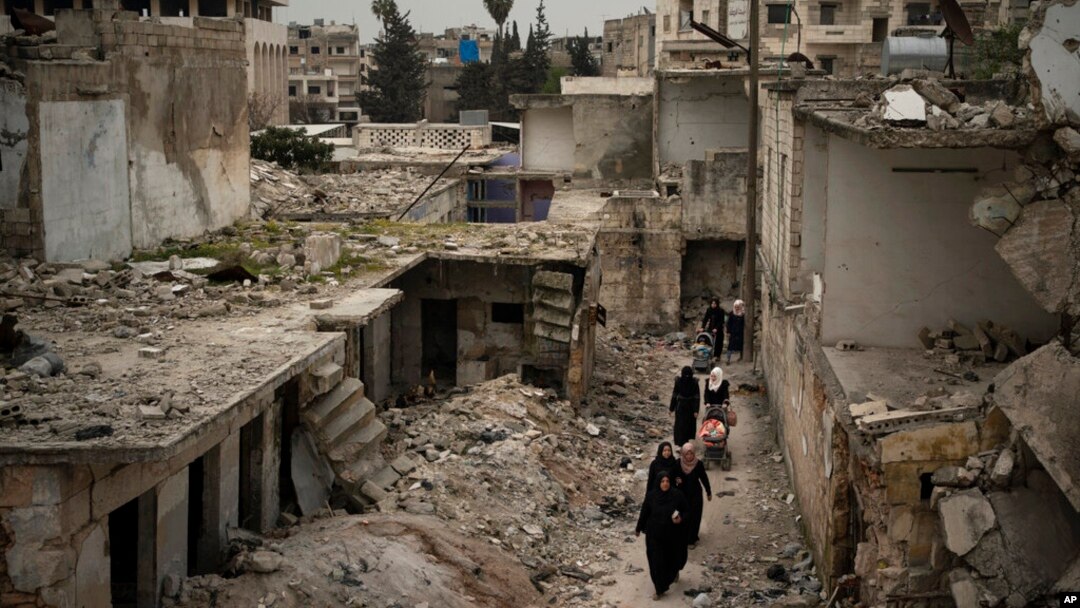 FILE - Women walk in a neighborhood heavily damaged by airstrikes in Idlib, Syria, March 12, 2020. 
