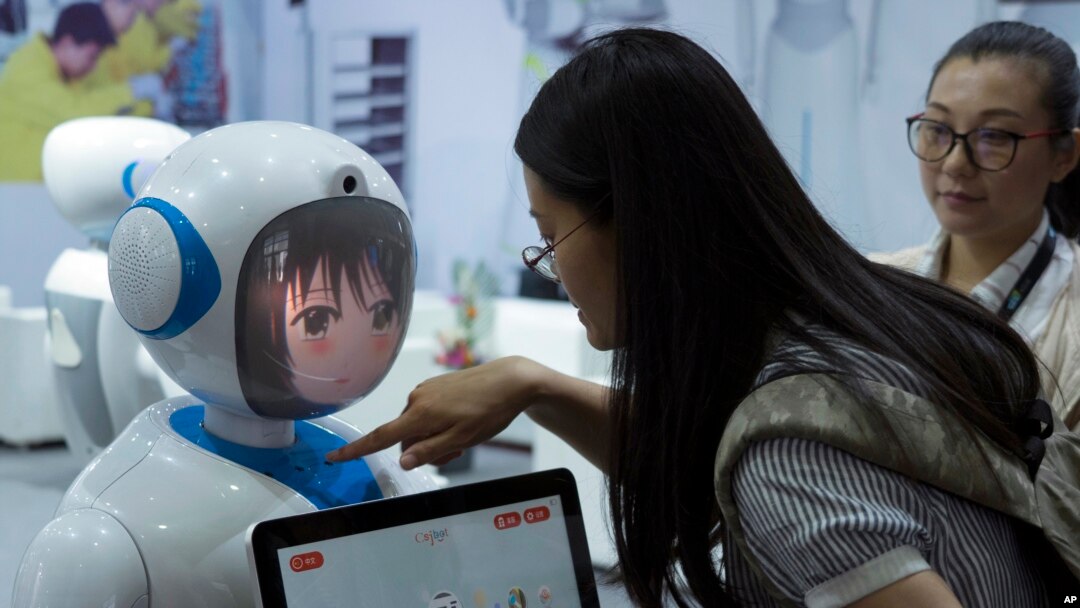 Women interact near a robot designed by Chinese robotics company Pangolin at the Consumer Electronics Show Asia 2018 in Shanghai, China, June 15, 2018. President Donald Trump is hiking the price of Chinese-made forklift trucks and X-ray machines for American buyers. They are part of a $50 billion list of Chinese exports targeted for a 25 percent tariff hike in response to complaints Beijing steals or pressures foreign companies to hand over technology. 