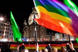 FILE - Far-right Pegida demonstrators, in background, wave flags in front of the Frauenkirche, while counterdemonstrators stand in the foreground, protesting against the far-right demonstration in Dresden, Germany, Feb. 17, 2020.