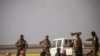 U.S.-backed Syrian Democratic Forces stand guard over men suspected of being Islamic State (IS) group fighters at a screening point outside Baghuz in eastern Syria, March 6, 2019.
