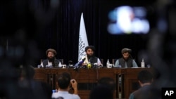 In front of a Taliban flag, Taliban spokesman Zabihullah Mujahid, center, speaks at a news conference, in Kabul, Afghanistan, Aug. 17, 2021. 