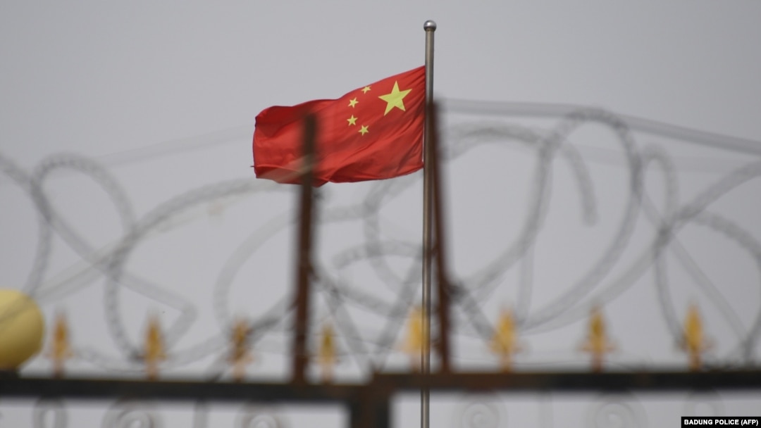 (FILES) This file photo taken on June 4, 2019 shows the Chinese flag behind razor wire at a housing compound in Yangisar, south of Kashgar, in China's western Xinjiang region. 