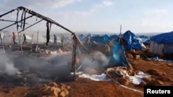 People walk though burnt tents at a camp for internally displaced people near Sarmada in Syria's Idlib province in this undated still image taken from video on May 6, 2016.