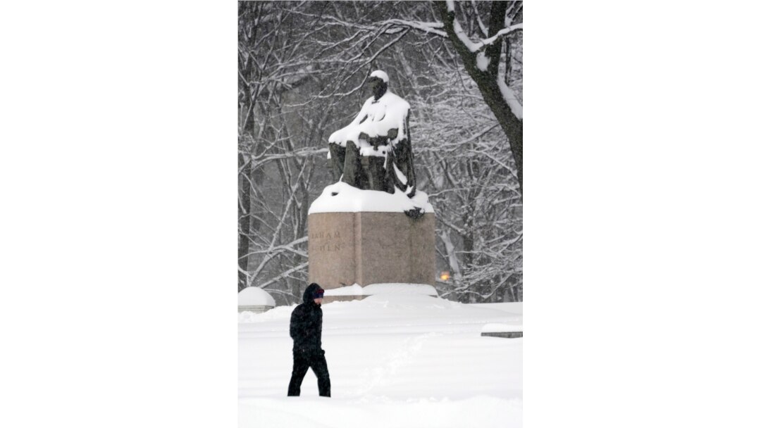 Un hombre solitario camina en una ligera tormenta de nieve a través del Grant Park de Chicago el domingo 31 de enero de 2021, pasando por una estatua nevada de Abraham Lincoln.