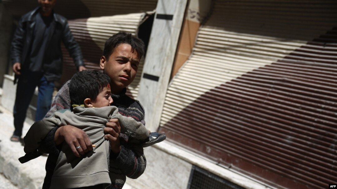 A Syrian boy carries a child while he runs for cover in the rebel-held area of Douma, east of the capital Damascus, as several air strikes pounded the city, April 22, 2015. 