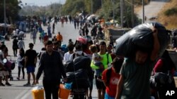 Migrants carry their belongings as they flee from Moria to the capital of Mytilene, on the northeastern island of Lesbos, Greece, Sept. 17, 2020.