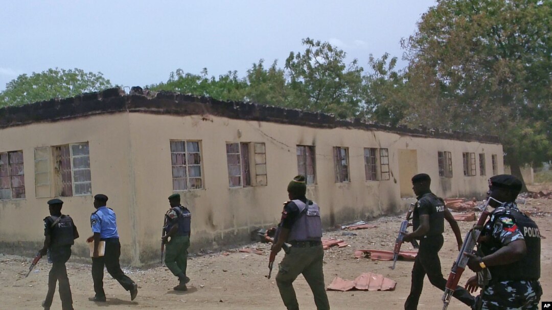 FILE - Security guards walk past a burned-out government secondary school in Chibok, Nigeria. April 21, 2014.