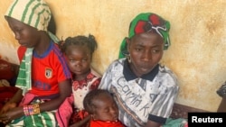 FILE - A woman who fled the violent rebellion in Central African Republic (CAR), sits with her family as they wait for their identification process in the border town of Garoua Boulai, Cameroon, Jan. 7, 2021.