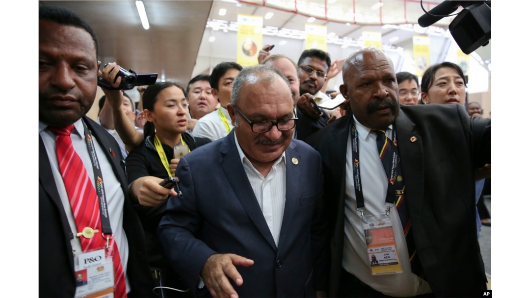 Papua New Guinea Prime Minister Peter O'Neill is escorted by security as he is pursued by reporters after reading his statement at the end of the APEC 2018 summit at Port Moresby, Papua New Guinea, Nov. 18, 2018.