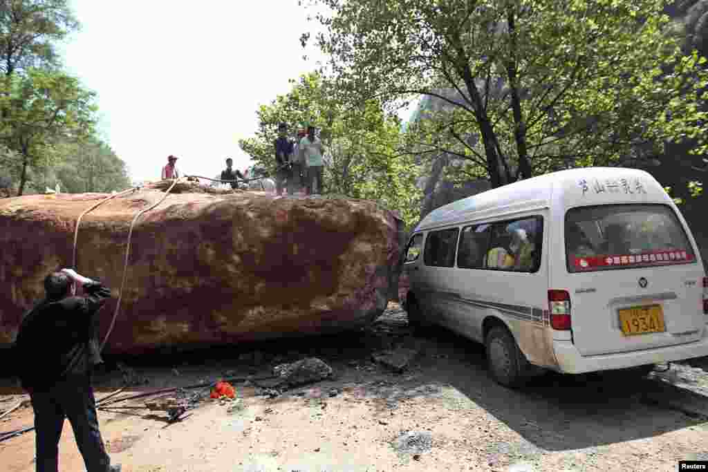 People stand near a van on a road blocked by a large rock after a strong 6.6 magnitude earthquake, at Longmen village, Lushan county, Ya'an, Sichuan province, Apr. 20, 2013.
