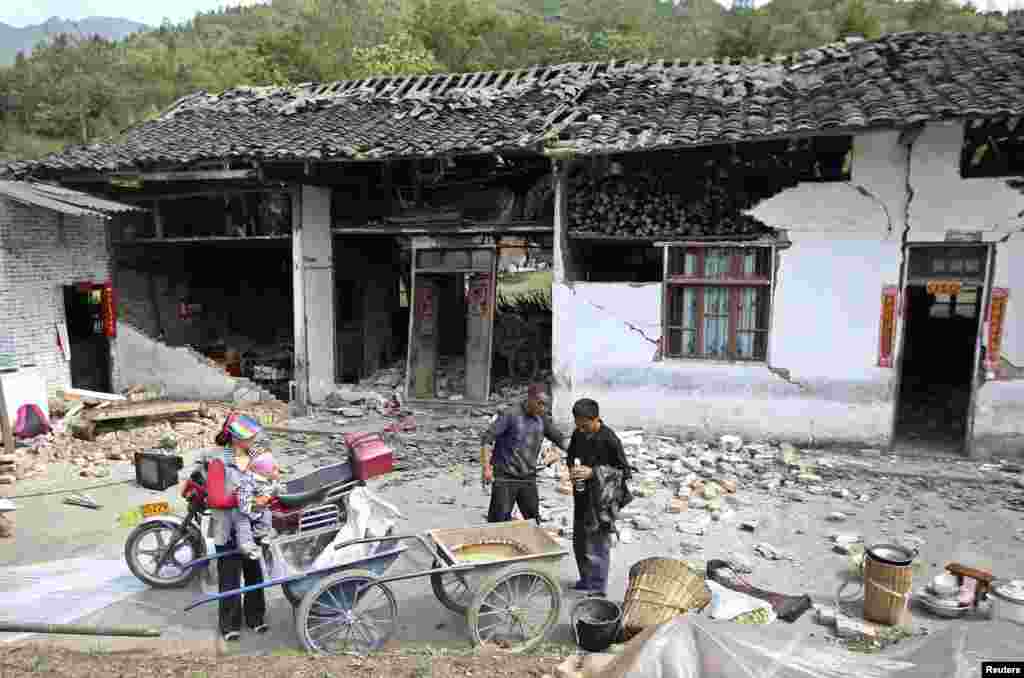 People stand outside a damaged house after a strong 6.6 magnitude earthquake hit, at Longmen village, Lushan county, Ya'an, Sichuan province, Apr. 20, 2013.
