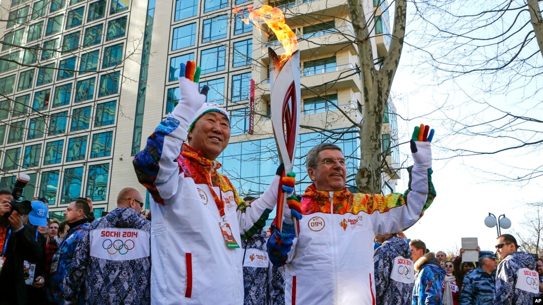 IOC President Thomas Bach, right, hands over the Olympic torch to United Nations Secretary-General Ban Ki-moon as the torch relay arrives in Sochi, ahead of the 2014 Winter Olympics, Feb. 6, 2014, in Russia.