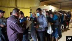 ARCHIVO - Varias personas hacen fila para abordar un autobús que los llevará al aeropuerto de San Antonio en un almacén manejado por el grupo sin fines de lucro Mission: Border Hope, operado por la Iglesia Metodista Unida, en mayo de 2022, en Eagle Pass, EEUU. 