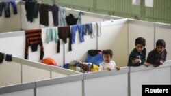 FILE - Children watch as they stand on beds in a shelter for migrants inside a hangar of the former Tempelhof airport in Berlin, Germany, Dec. 9, 2015. 