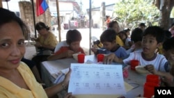 Lessons are over and a lunch of rice porridge with chicken and beans is served. Sitting at the 10-year olds' table, volunteer teacher Yolanda Penalosa shows off her student Ericson's quick progress in arithmetic, May 25, 2012. (S. Orendain/VOA)