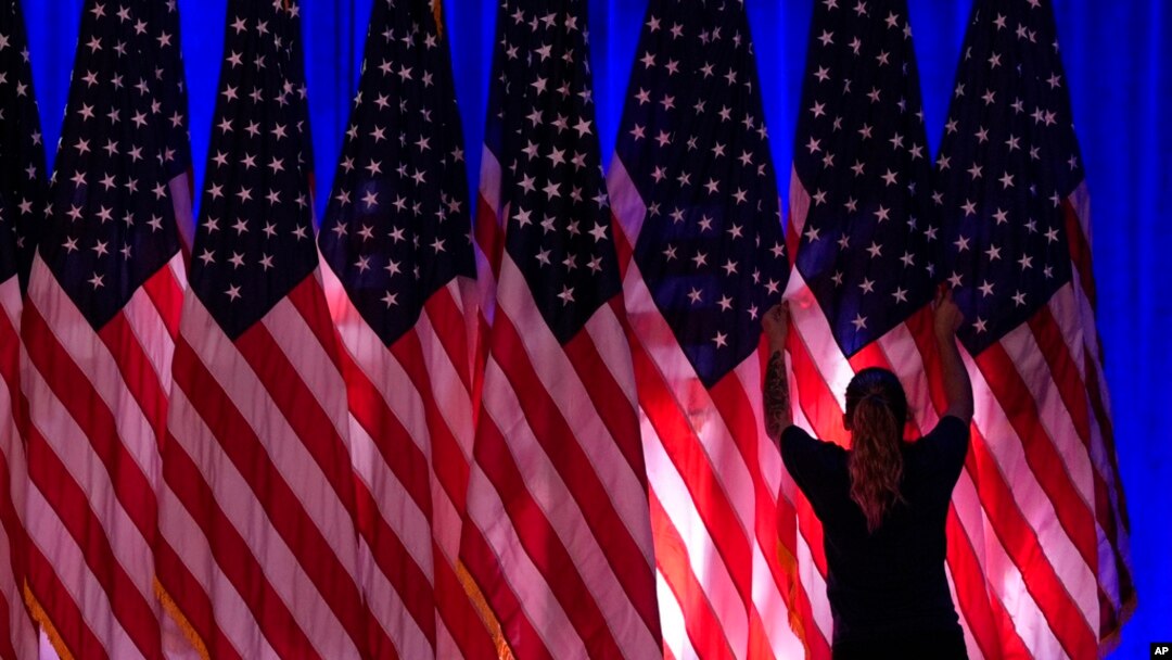 Un trabajador ajusta las banderas en el escenario antes de un evento en el comando de campaña del candidato presidencial republicano Donald Trump, en West Palm Beach, Florida, el 5 de noviembre de 2024.