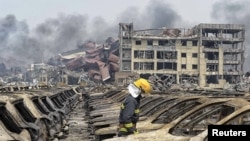 A firefighter walks among damaged vehicles as smoke rises amidst shipping containers at the site of explosions, at Binhai new district in Tianjin, China, Aug. 14, 2015.
一名消防员在烧毁的车辆中行走（2015年8月14日）。