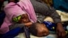 FILE - A mother sleeps with her child holding a toy gun, outside the UN refugee agency in Cape Town, South Africa, Oct. 10, 2019.