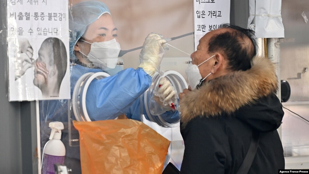 A medical staff member (L-in booth) takes a nasal swab from a visitor as part of a test for the Covid-19 coronavirus at a virus testing center in Seoul on Jan. 26, 2022.