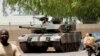 People drive past a Chad army tank near the presidential palace, as fighters from the rebel Front for Change and Concord in Chad (FACT) appeared to be moving toward the capital, according to the United States, in N'djamena, Chad, April 19, 2021. 
