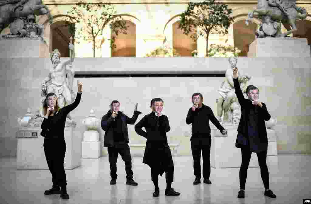 Members of the international climate activist movement 350.org wear masks depicting French energy giant Total chief executive Patrick Pouyanne in the Marly courtyard of the Louvre museum in Paris to protest against the Louvre and Total partnership.