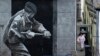 FILE - A woman takes out her rubbish beside a mural depicting a British soldier knocking down the door of a house with a sledge hammer in Derry, Northern Ireland, March 23, 2010. The Bloody Sunday massacre took place in Derry in 1972.