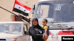 FILE - A Syrian refugee who left Lebanon carries a toddler as she arrives in Qalamoun, Syria, June 28, 2018.