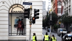 Limpiadores pasan al lado de una tienda Chanel en el distrito comercial central de Melbourne el 11 de mayo de 2020 cuando Australia comienza a aliviar sus restricciones contra el coronavirus COVID-19.
