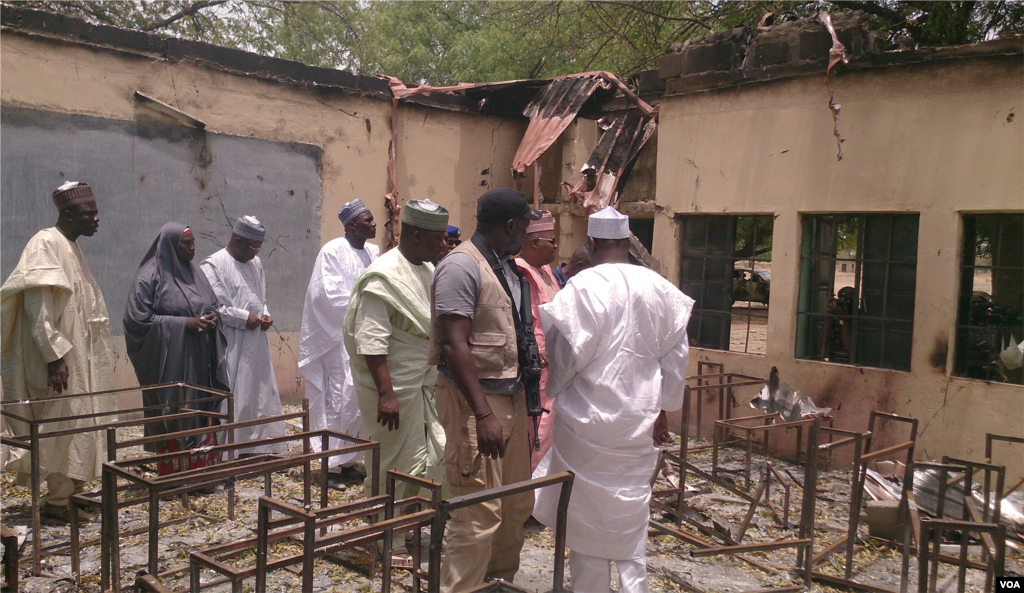O Governador de Chibok (vestido de rosa), o comissário local para a educação (o quarto a partir da esquerda) com a segurança armada e residentes de Chibok, inspeccionam a escola que foi incendiada depois de mais de 200 terem sido raptadas por homens armados, Chibok, Nigéria, Abril 21, 2014. (Anne Look/VOA)