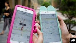China ride-hailing apps: Women holding their smartphones show the ride-hailing apps Uber Technology Ltd., left, and Didi Chuxing at a residential compound in Beijing, Monday, Aug. 1, 2016.