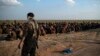 FILE - U.S.-backed Syrian Democratic Forces fighters stand guard next to men waiting to be screened after being evacuated out of the last territory held by Islamic State group militants, near Baghuz, eastern Syria, Feb. 22, 2019.