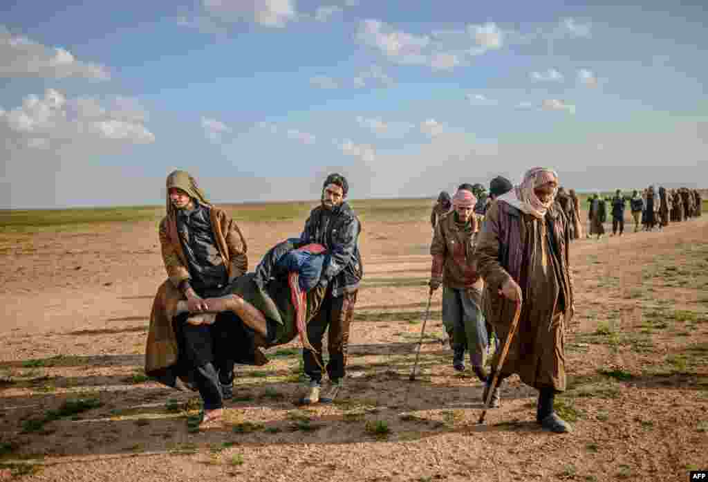 Men suspected of being Islamic State (IS) fighters carry a wounded man as they walk toward the Kurdish-led Syrian Democratic Forces after leaving the IS group's last holdout of Baghouz in Syria's northern Deir Ezzor province.