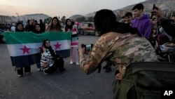 A Syrian opposition fighter takes pictures for citizens who carry the revolutionary flag as they celebrate during the second day of the take over of the city by the insurgents in Damascus, Syria, Dec. 9, 2024. 
