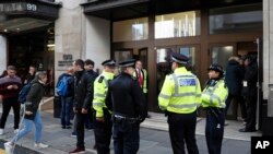 Police officers and security watch as people re-enter a building after a stabbing incident in central London, Friday, Nov. 2, 2018. 