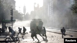 People and demonstrators run as a riot police vehicle uses a water cannon during a protest against Chile's government in Santiago, Chile, Oct. 29, 2019.