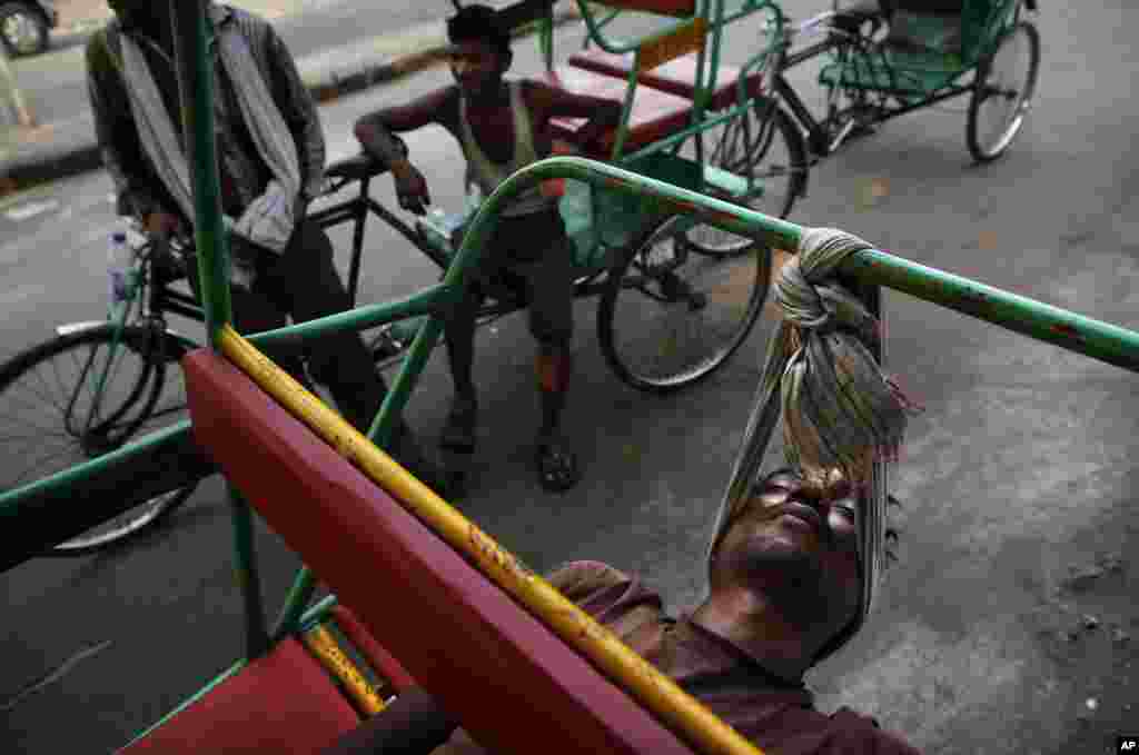 An Indian bicycle rickshaw walla uses a scarf to rest his head while sleeping on his rickshaw in New Delhi. 