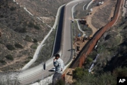FILE - A man looks out at the U.S. border where workers are replacing parts of the U.S. border wall for a higher one, in Tijuana, Mexico, Dec. 19, 2018.